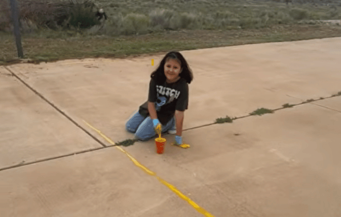 Young female student painting a line on the school grounds. 