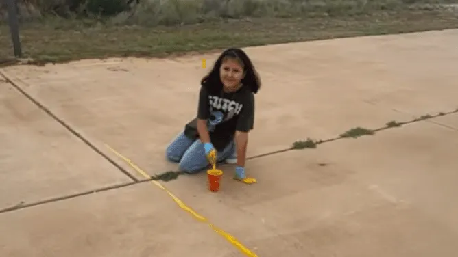 Young female student painting a line on the school grounds. 